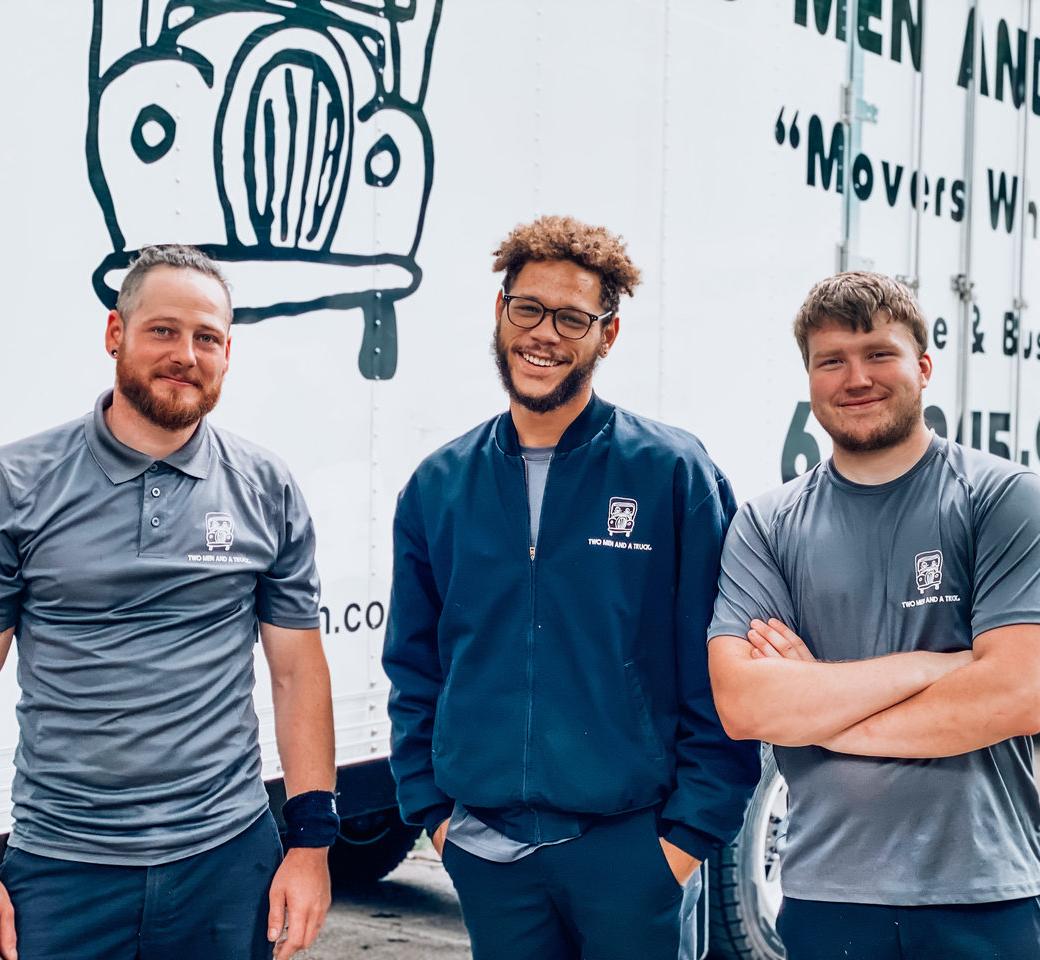 Three movers standing in front of a moving truck smiling